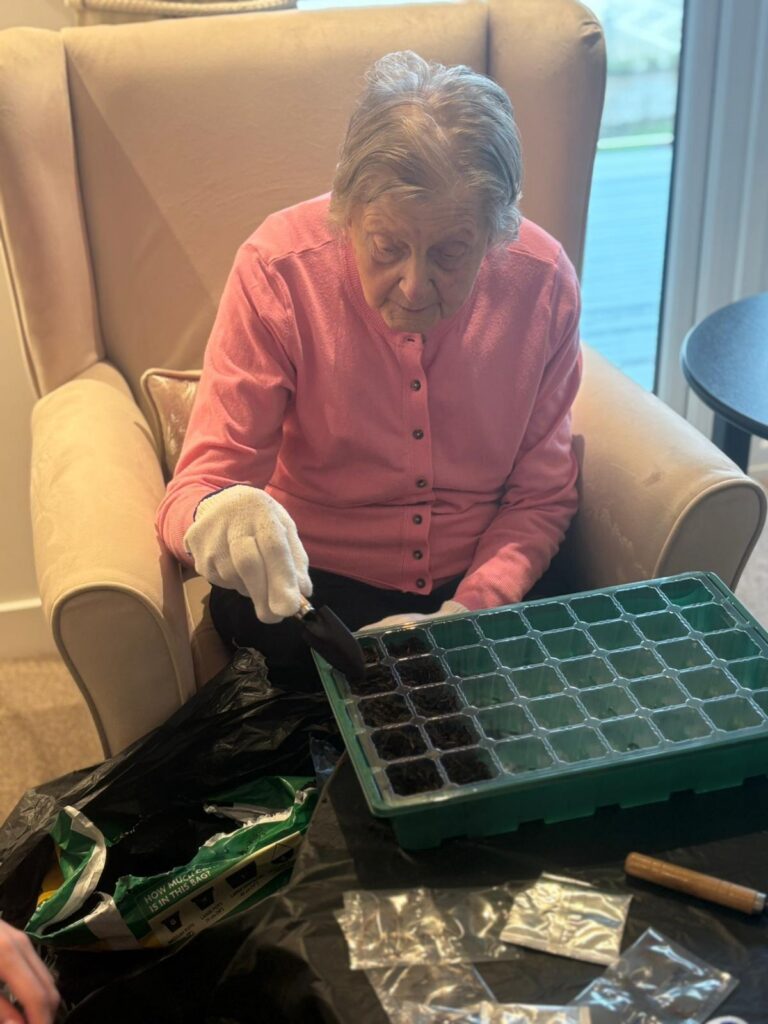 elderly woman sitting indoors planting seeds in soil