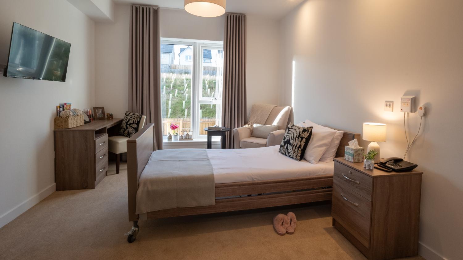 care home bedroom with single profiling bed and wooden furniture