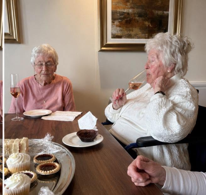 older ladies at a table drinking champagne with some cakes