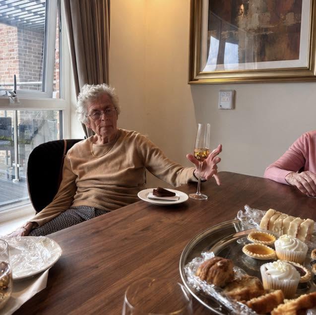 older lady sat at a table holding a glass of champagne